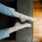 Beige KLUE lurex socks worn with turned-up jeans, feet resting on a green corduroy sofa