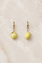 Gold huggie hoop earrings with a bright yellow enamel lemon charm hanging from each hoop