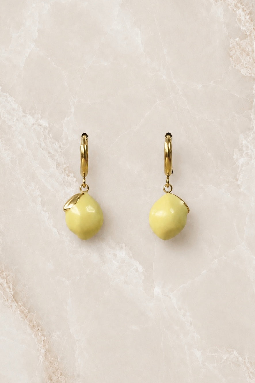 Gold huggie hoop earrings with a bright yellow enamel lemon charm hanging from each hoop