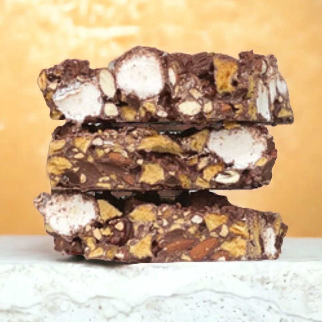 Three stacked slices of honeycomb rocky road showing marshmallow, honeycomb and almond pieces in milk chocolate