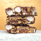 Three stacked slices of honeycomb rocky road showing marshmallow, honeycomb and almond pieces in milk chocolate