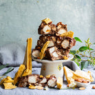 Chunks of Honeycomb Highway rocky road piled on a white cake stand with honeycomb shards and almonds