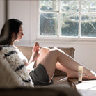 Woman applying Salus Geranium & Bergamot hand cream while relaxing on a sofa in window light