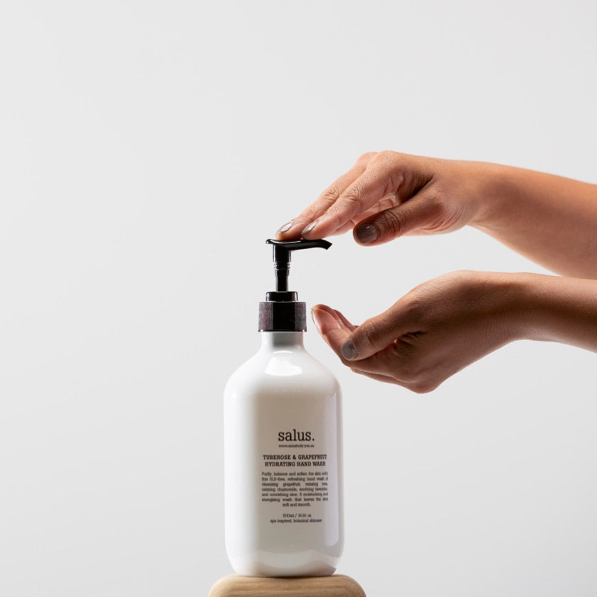 Hands pressing the pump of a Salus Tuberose & Grapefruit Hydrating Hand Wash bottle