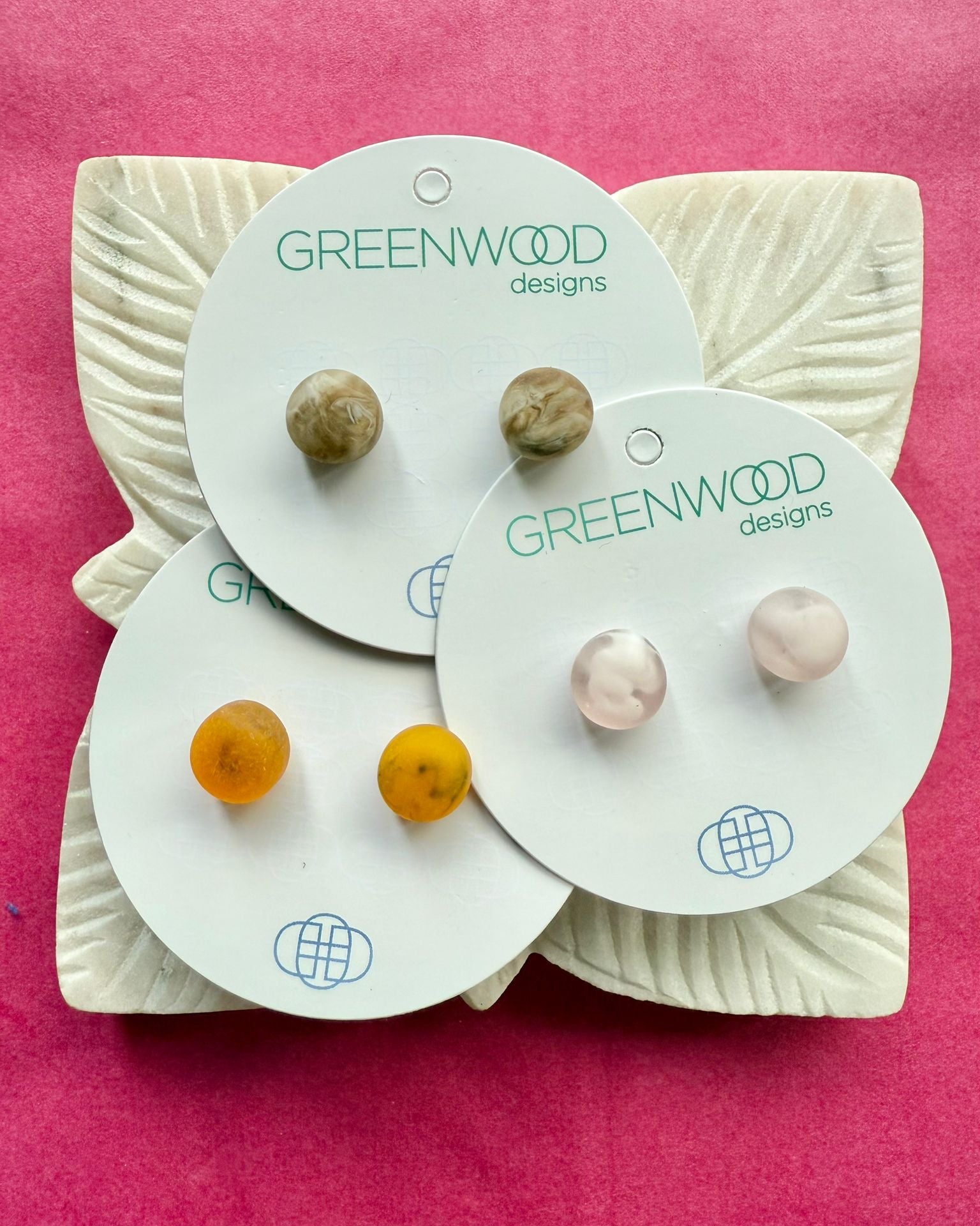 Round resin studs in Horn Marble, Light Pink Marble and Tortoiseshell on overlapping cards, on a carved white leaf dish.