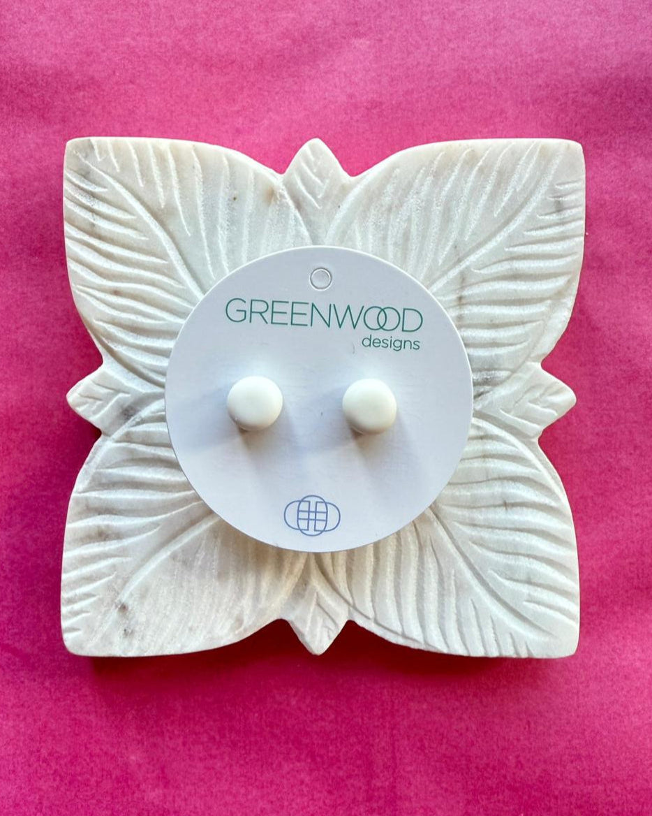 Round earrings in White: a pair of white resin studs on a round card, on a carved white leaf dish against pink paper.