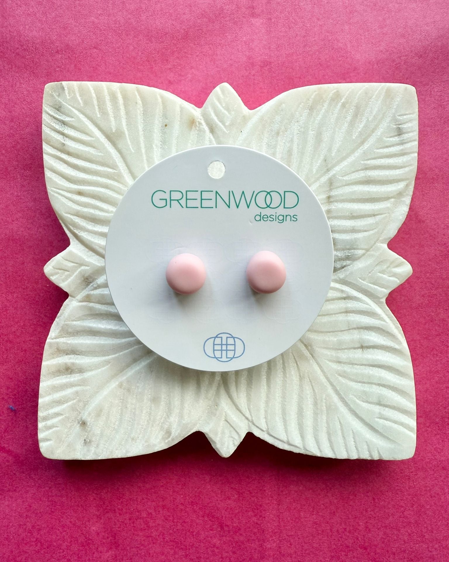 Round earrings in Baby Pink: a pair of pale pink resin studs on a round card, on a carved white leaf dish against pink paper.