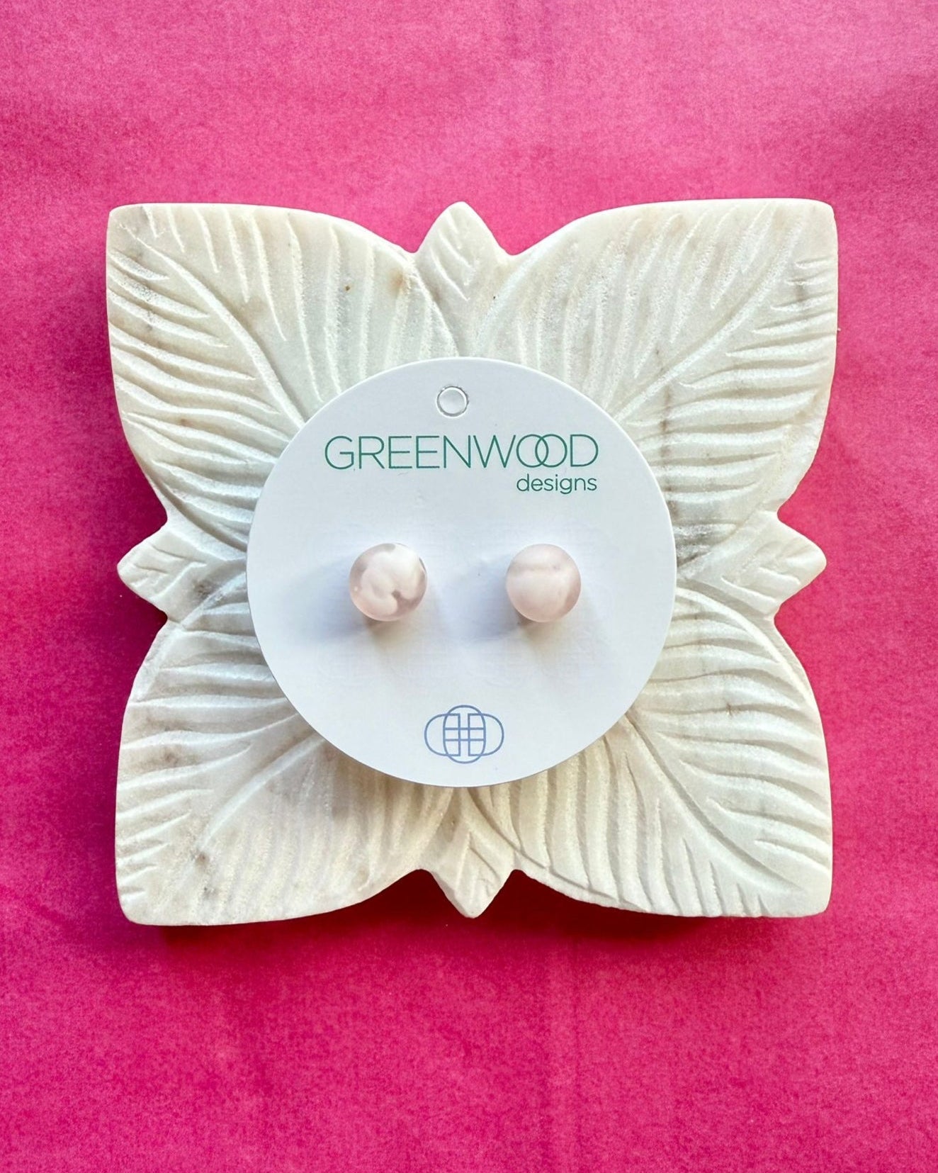 Round earrings in Light Pink Marble: a pair of translucent pink and white marbled resin studs on a round card, on a carved white leaf dish against pink paper.