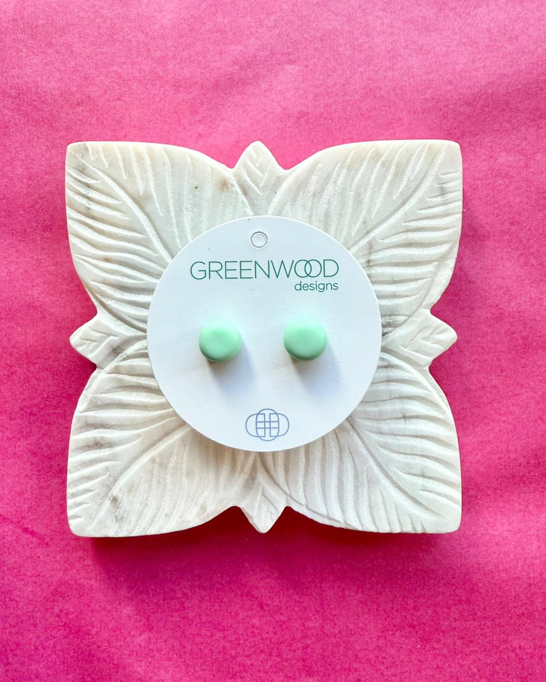 Round earrings in Mint: a pair of pale mint-green resin studs on a round card, on a carved white leaf dish against pink paper.