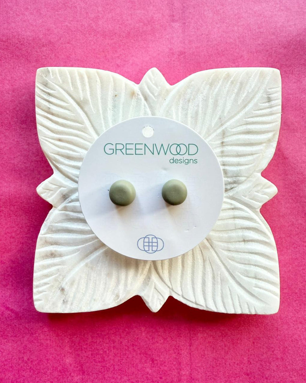 Round earrings in Moss: a pair of muted sage-green resin studs on a round card, on a carved white leaf dish against pink paper.