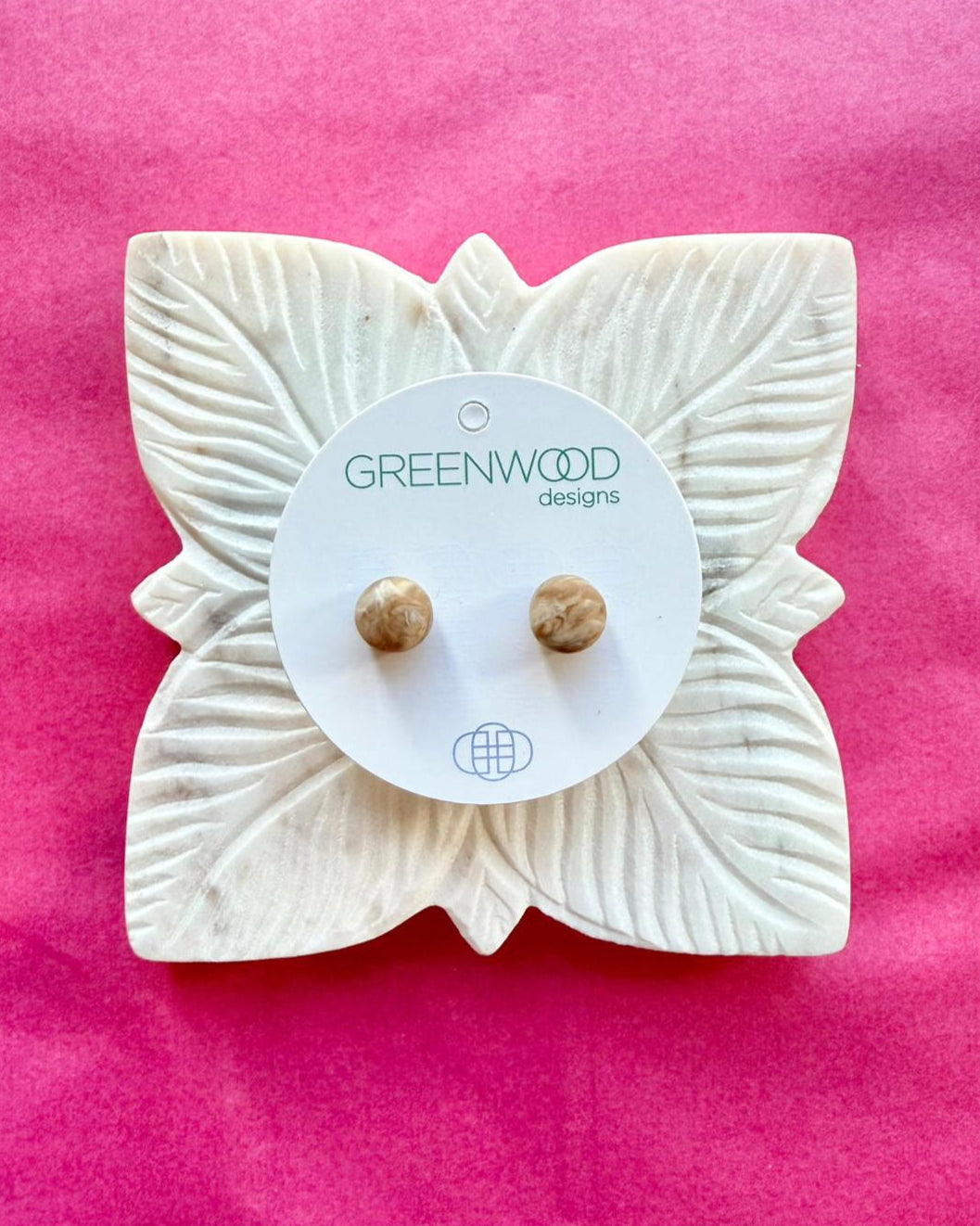 Round earrings in Horn Marble: a pair of cream and caramel marbled resin studs on a round card, on a carved white leaf dish against pink paper.