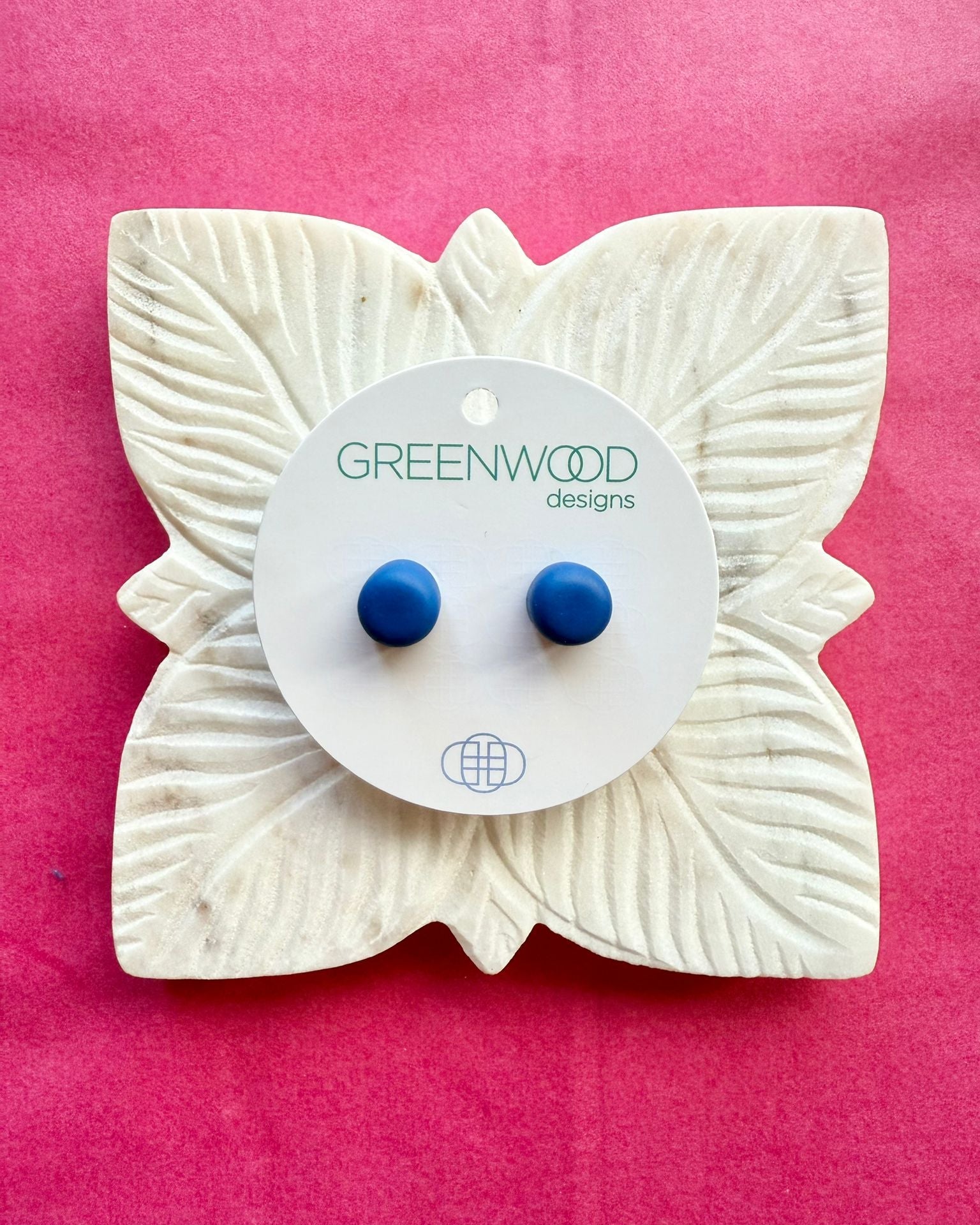 Round earrings in Royal Blue: a pair of bright cobalt-blue resin studs on a round card, on a carved white leaf dish against pink paper.