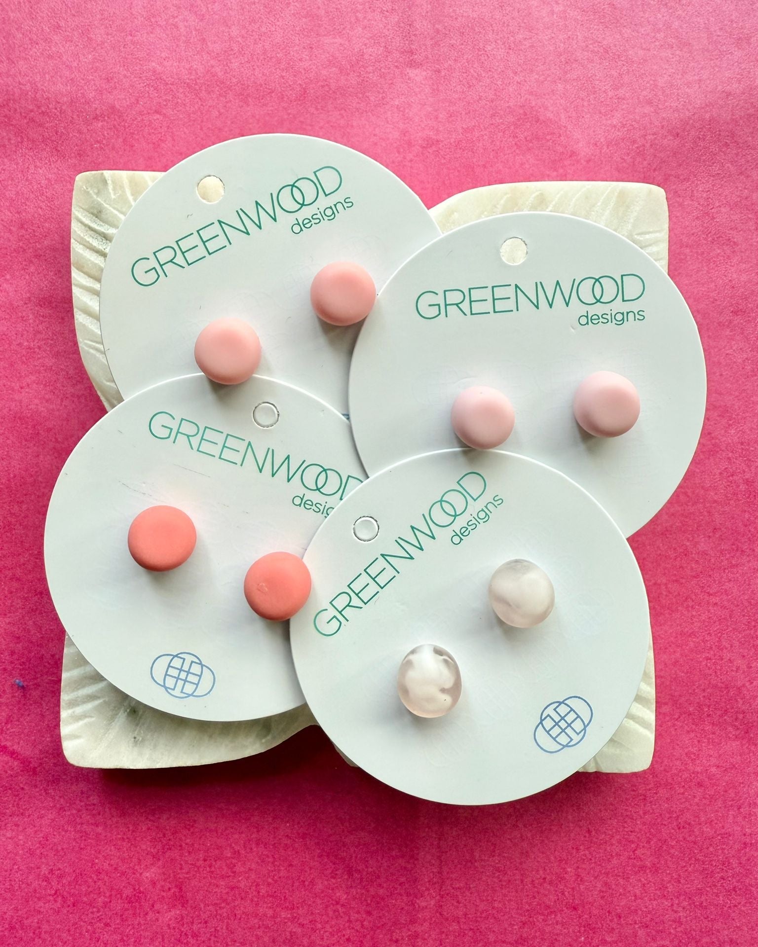 Four pairs of round resin studs in pale pinks, coral and Light Pink Marble on overlapping cards, on a carved white leaf dish.