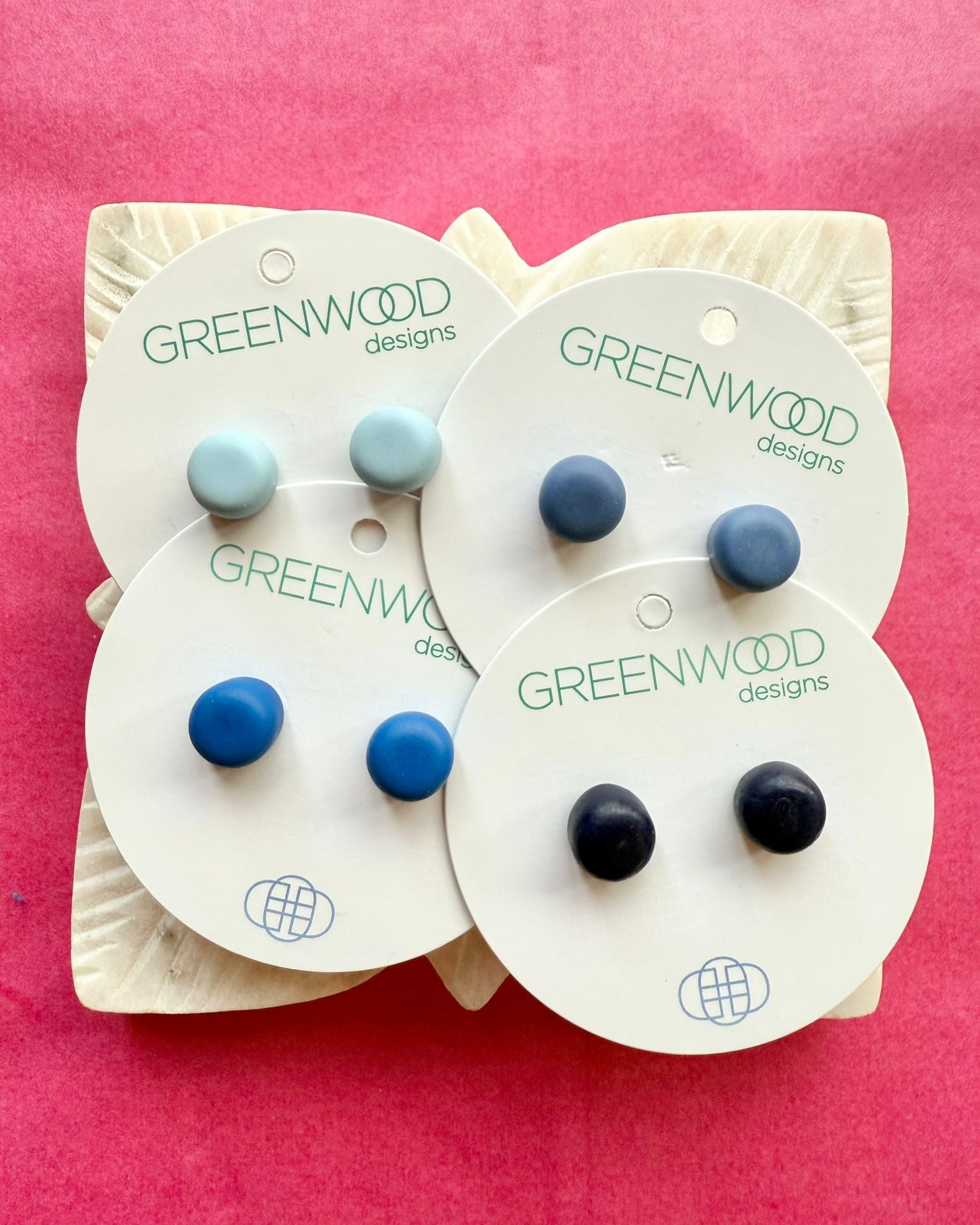 Round resin studs in Baby Blue, a mid denim blue, Royal Blue and Navy on overlapping cards, on a carved white leaf dish.