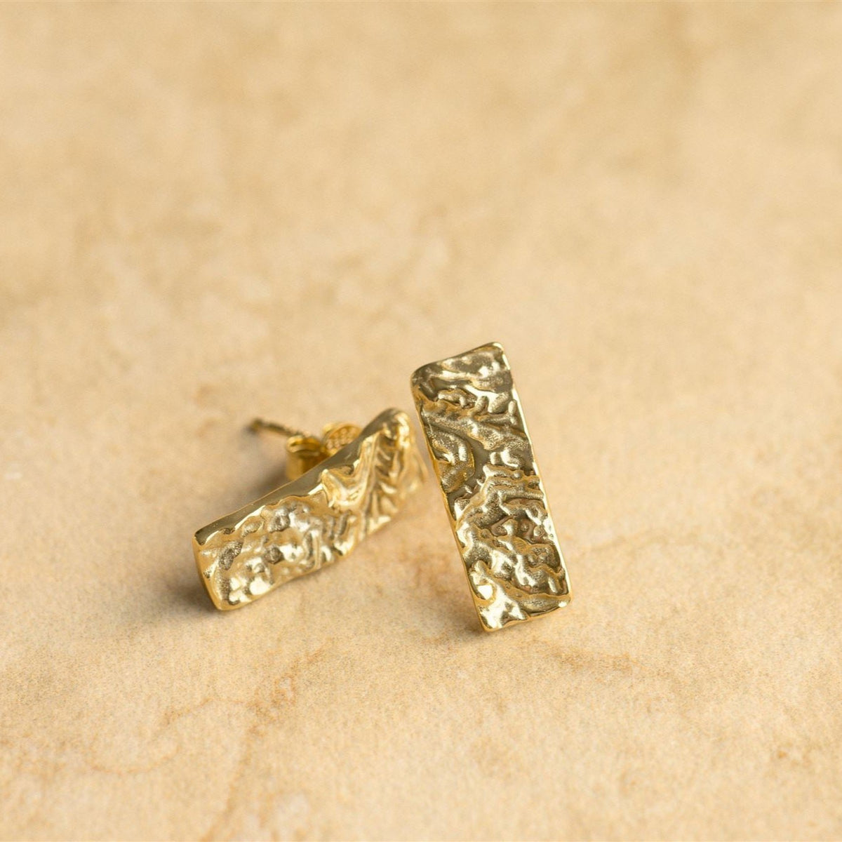 Bella gold earrings resting on sandstone, one on its side showing the post