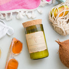 Coconut & Lime candle on a pink tasselled towel with orange sunglasses, a string bag of citrus and a coconut