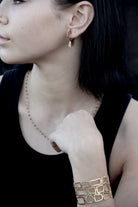 Model in a black top wearing the wide gold lattice cuff, with drop earrings and a fine beaded necklace
