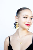 Smiling model in a black top wearing the gold triple-disc earring and a fine gold necklace