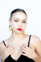 Model with red lipstick, hands at her chest, wearing the gold triple-disc earrings