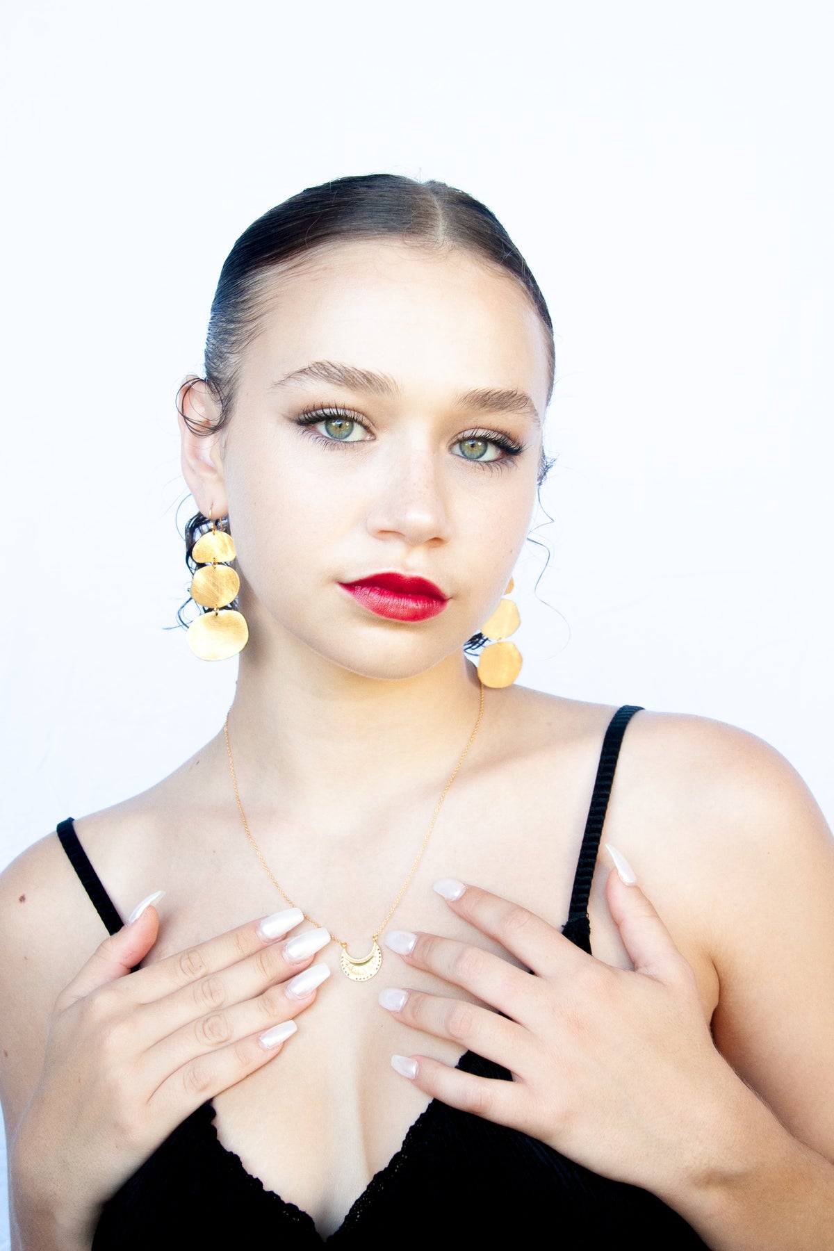 Model with red lipstick, hands at her chest, wearing the gold triple-disc earrings