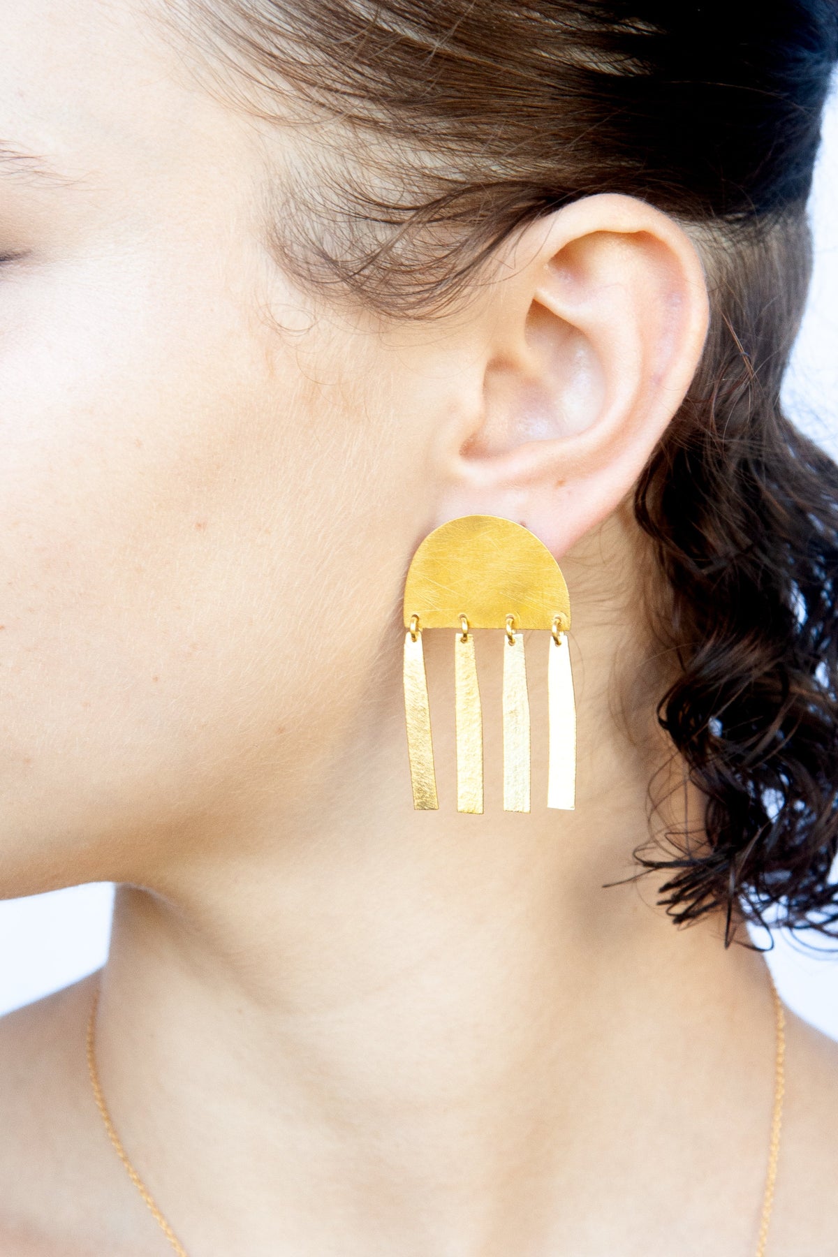 Close-up of the gold half-moon bar earring worn with dark curly hair