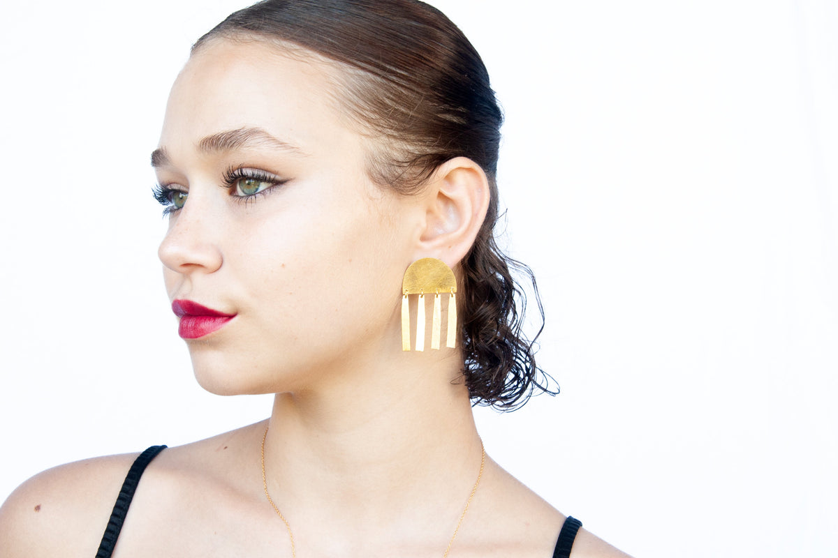 Model in a black strappy top wearing the gold half-moon bar earring, head turned to the side