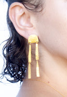 Close-up of the gold arch bar-drop earring worn with dark curly hair