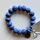 Rock bracelet in Indigo: a stretch bracelet of chunky cornflower blue resin beads with its swing tag and metal charm, laid on a pale surface.