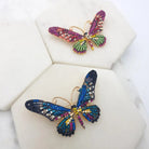 Two crystal butterfly brooches, one in pink and green and one in blue and multicolour, on white marble