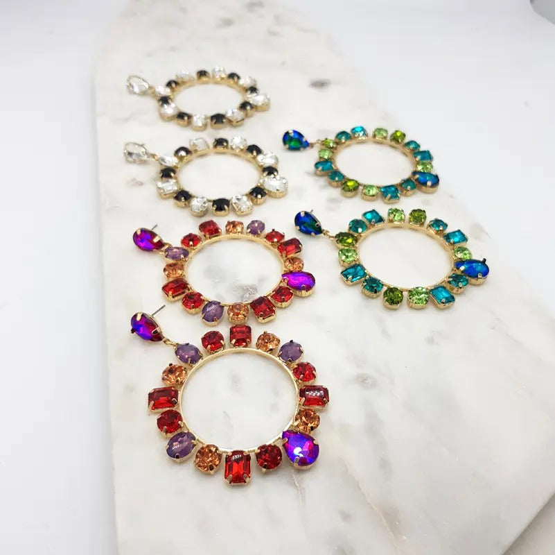 Five pairs of crystal circle drop earrings in assorted colours including red, black, green and clear, on marble