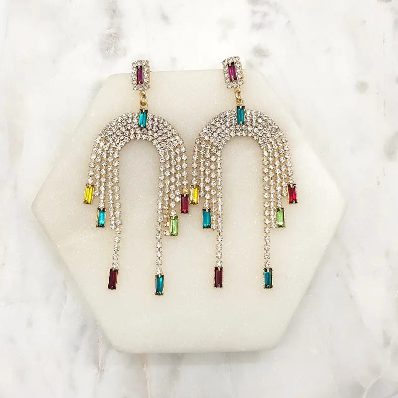 Pair of gold-tone arch earrings covered in clear crystals with multicoloured baguette crystal fringe drops, on marble