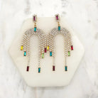 Pair of gold-tone arch earrings covered in clear crystals with multicoloured baguette crystal fringe drops, on marble
