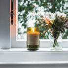 Lit Coconut & Lime candle on a windowsill beside a glass jar of dried flowers