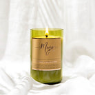 Close-up of the lit Cucumber & Muddled Mint candle in its green reclaimed wine bottle against white linen