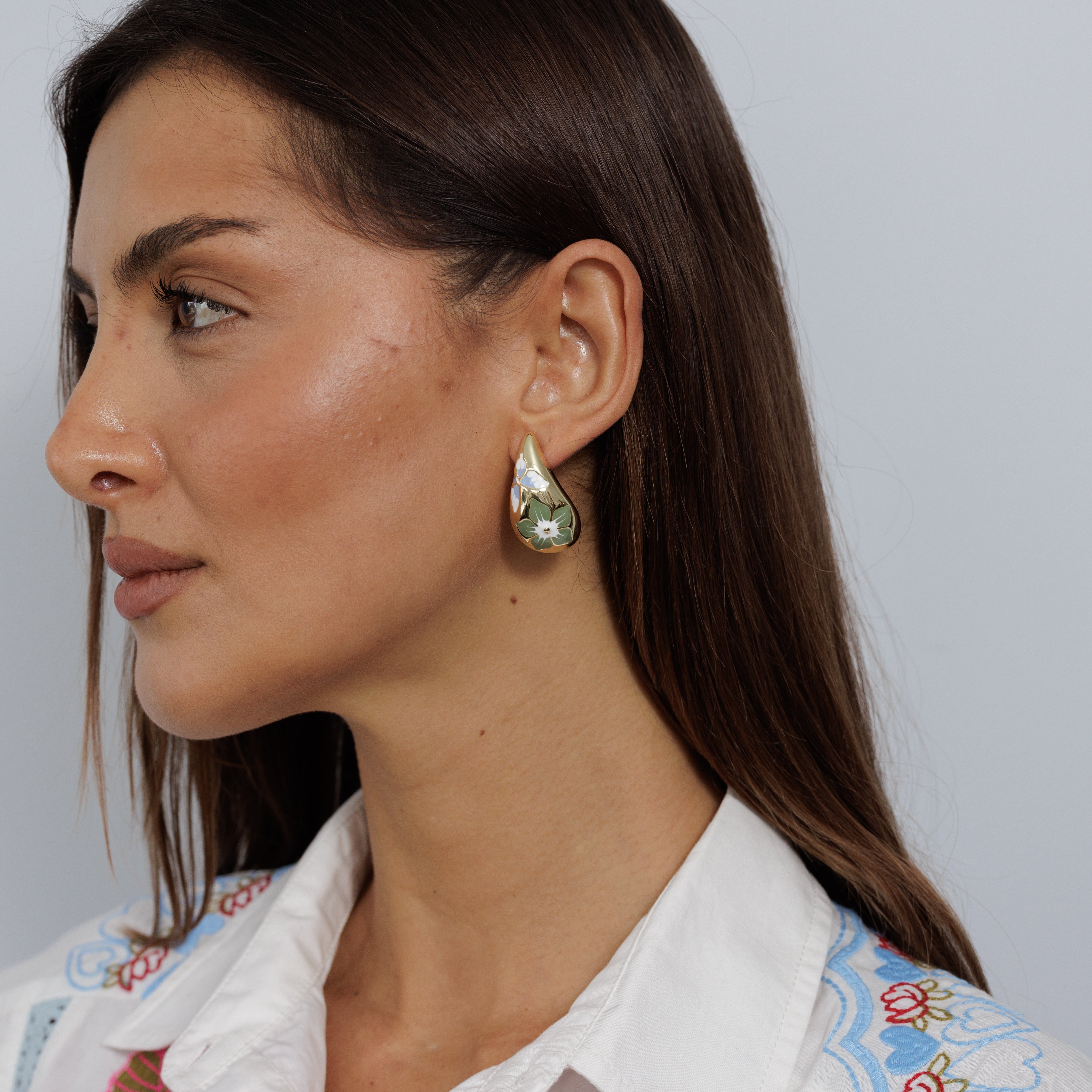A model wearing the gold teardrop earring painted with a green flower, seen in profile.