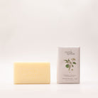 Cream shea butter soap bar beside its pale grey box, printed with green leaves and seed heads and labelled Bergamot, Tangerine & Geranium Leaf.