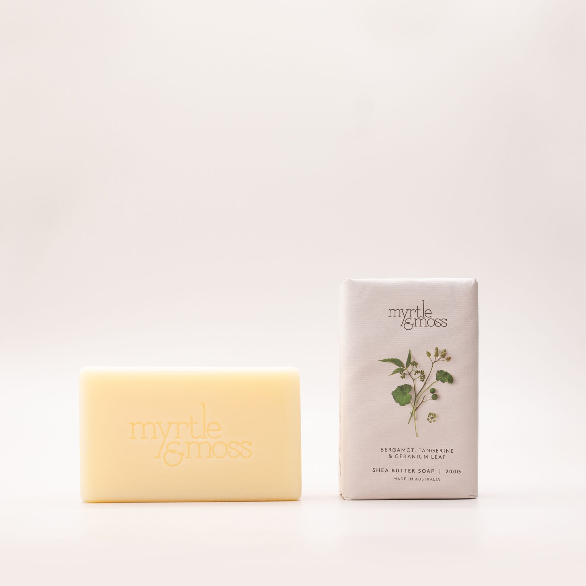 Cream shea butter soap bar beside its pale grey box, printed with green leaves and seed heads and labelled Bergamot, Tangerine & Geranium Leaf.