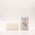 Cream shea butter soap bar beside its pale grey box, printed with deep red and pink pressed blooms and labelled Rose Geranium, Grapefruit & Clary Sage.