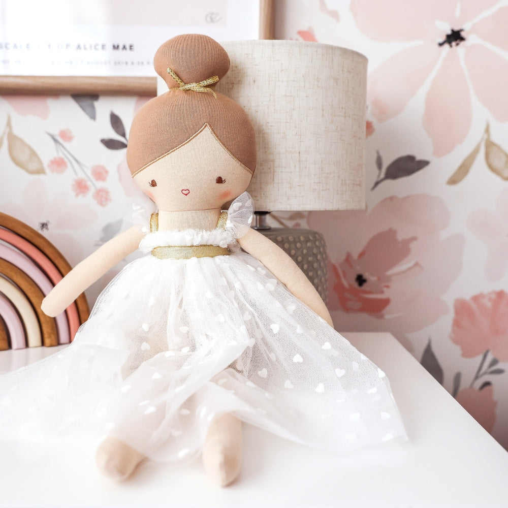 Lottie doll seated beside a lamp against pink floral wallpaper