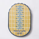 Oval mango wood wall plaque with a navy scalloped edge, a column of blue sardines down a yellow and white stripe, and packed with love in navy lettering at the base