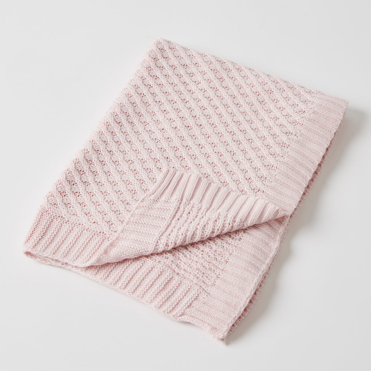 Pale pink knitted baby blanket folded on white, showing its raised basket-weave texture and ribbed border