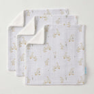 Three white muslin face washers fanned out, printed with small cream ducks and reeds, corners turned back to show soft cream towelling, a small blue tag on one edge