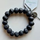 Rock bracelet in Navy: a stretch bracelet of chunky dark navy resin beads with its swing tag and metal charm, laid on a pale surface.