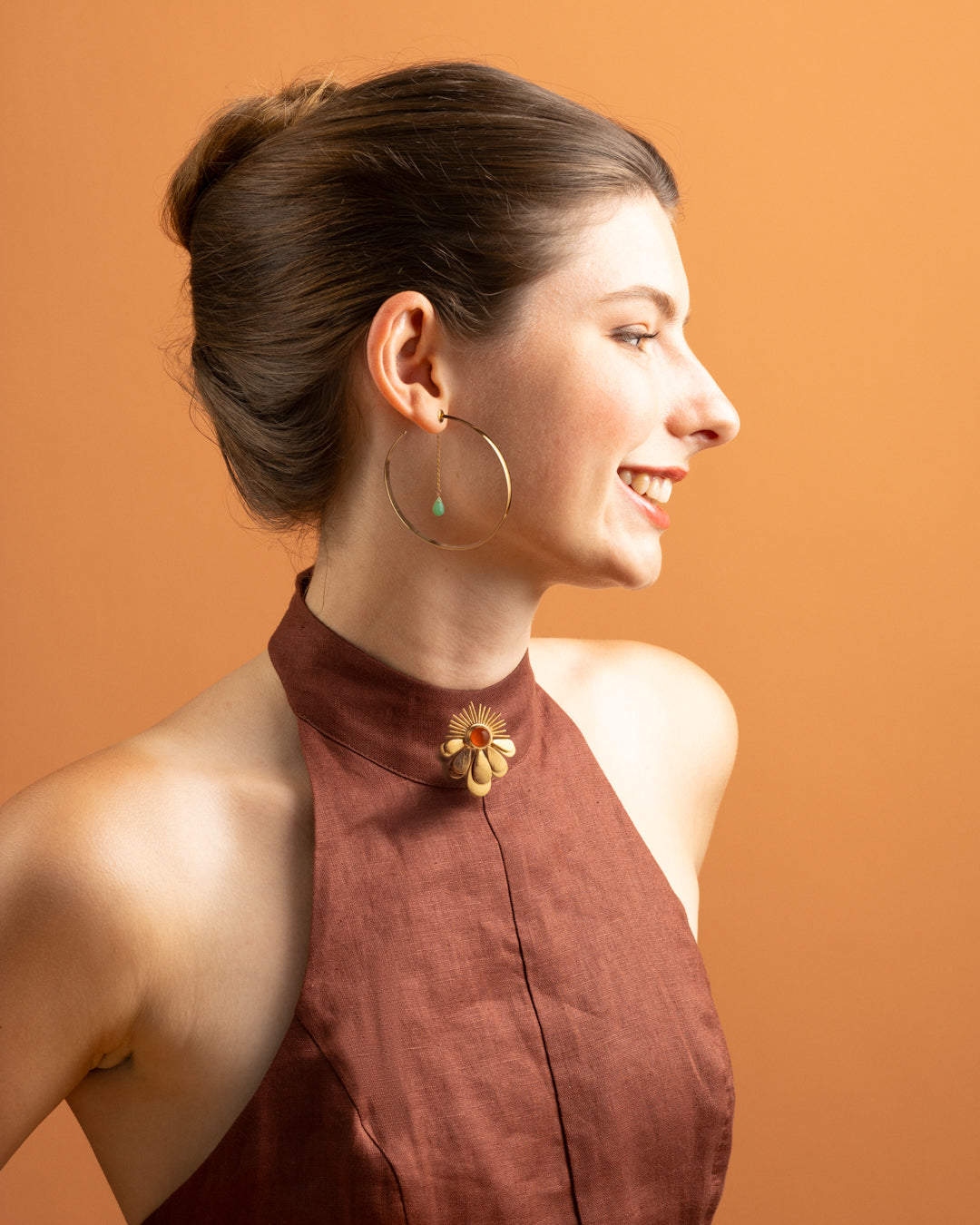 Model in profile wearing a Euro Gold hoop earring with gem drop, orange backdrop