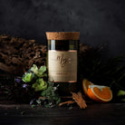 Oakmoss & Sage candle in a reclaimed wine bottle styled with cork bark, herbs and orange on a dark bench