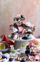 Pavlova Parkway rocky road chunks stacked on a white cake stand with meringues, blueberries and passionfruit