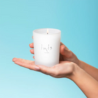 Lit Inis Scented Candle held in two cupped hands against a pale blue background