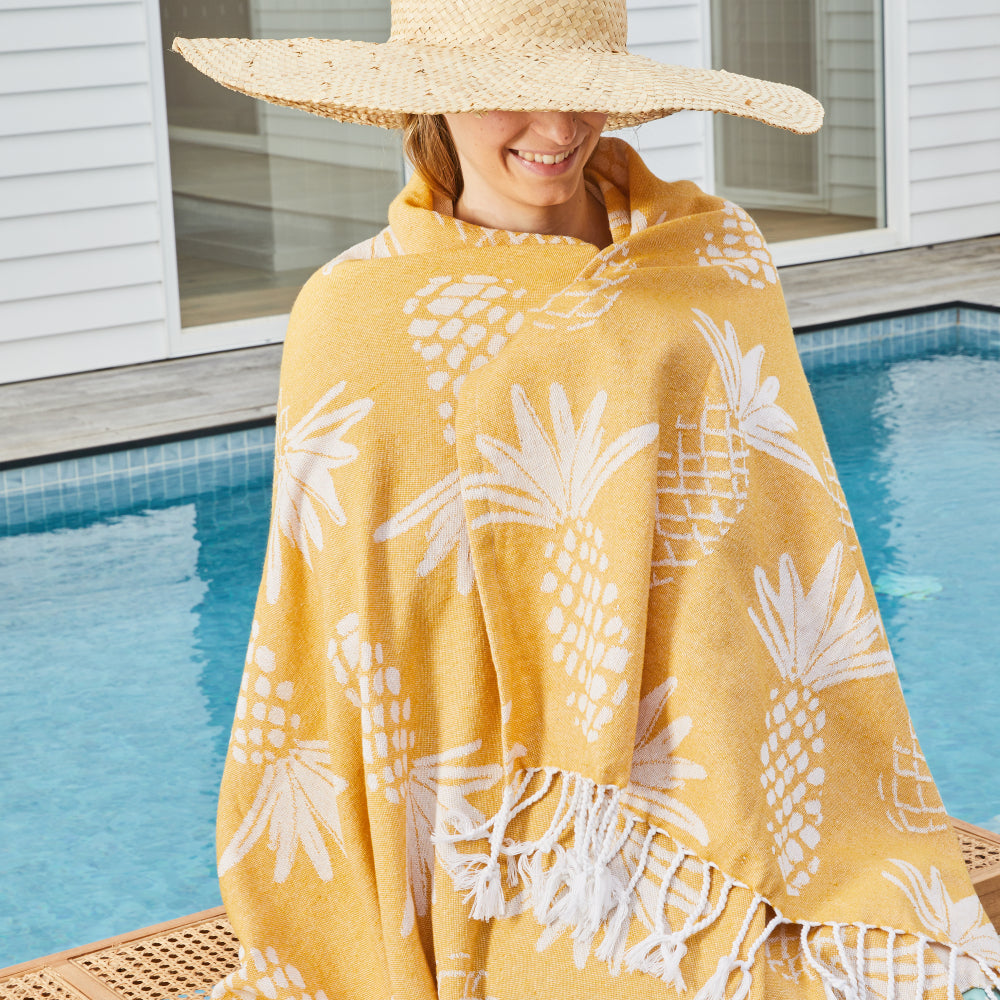 Woman in a sun hat wrapped in the yellow Pineapple Turkish towel by a pool