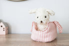 Marshmallow puppy plush in its pink striped carrier on a wooden shelf