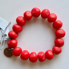 Rock bracelet in Red: a stretch bracelet of chunky bright red resin beads with its swing tag and metal charm, laid on a pale surface.